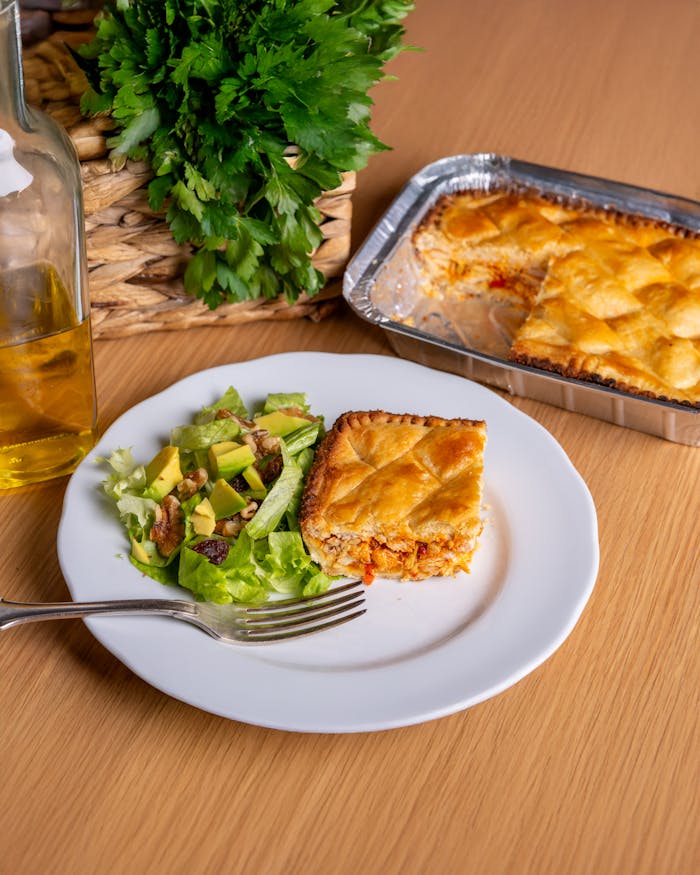 Delicious golden-brown pie with a fresh green salad and olive oil on a wooden table.
